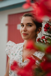 Photographie d'une femme à côté de fleurs rouges.